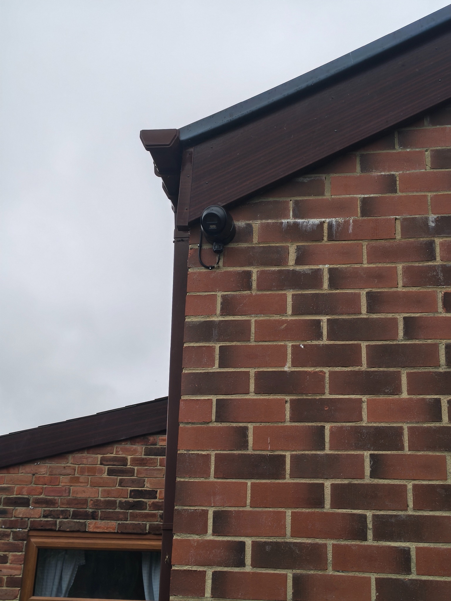 Small CCTV camera fitted beneath the roofline of a brick building