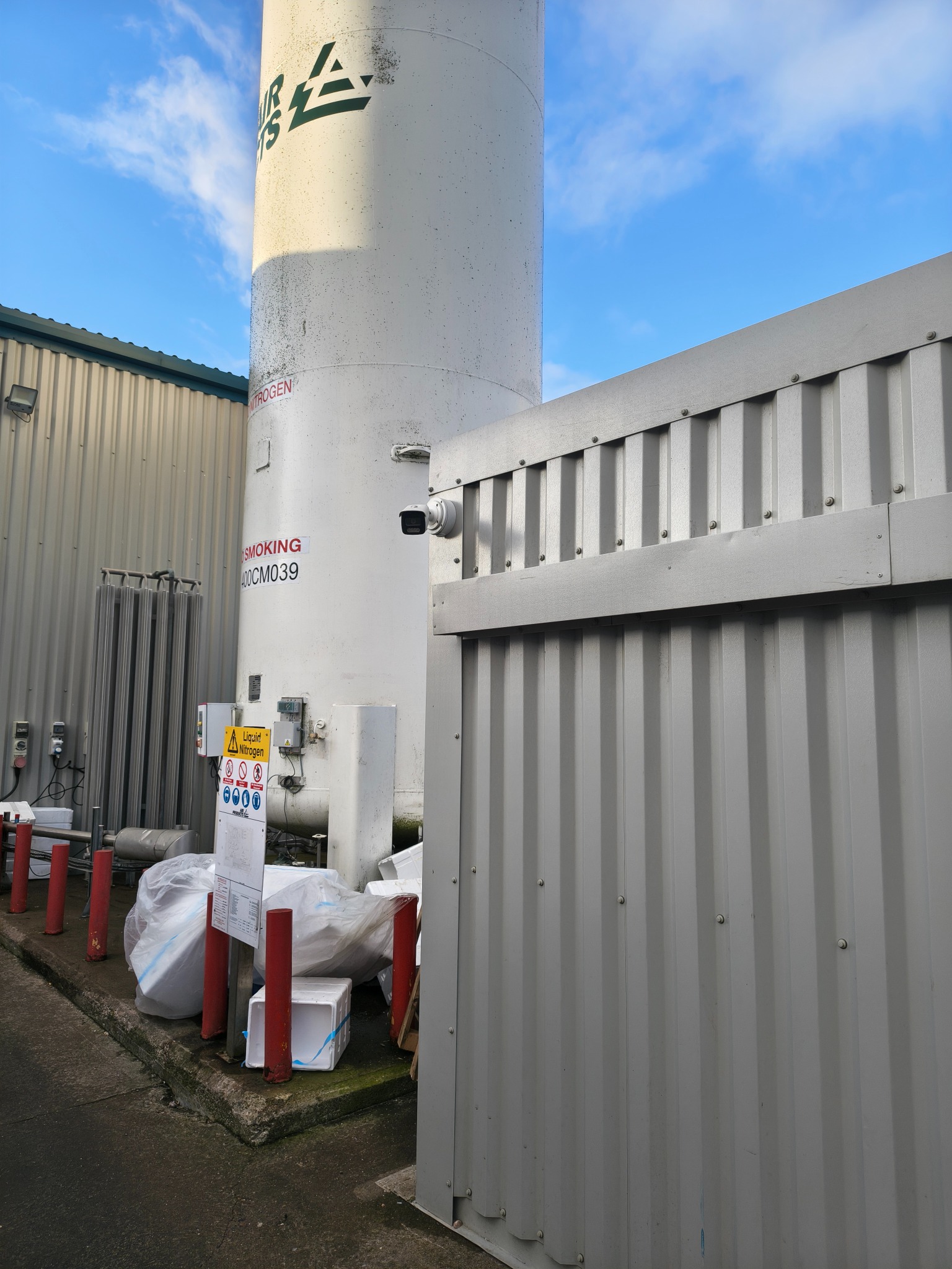 CCTV camera mounted on a corrugated building beside an industrial tank