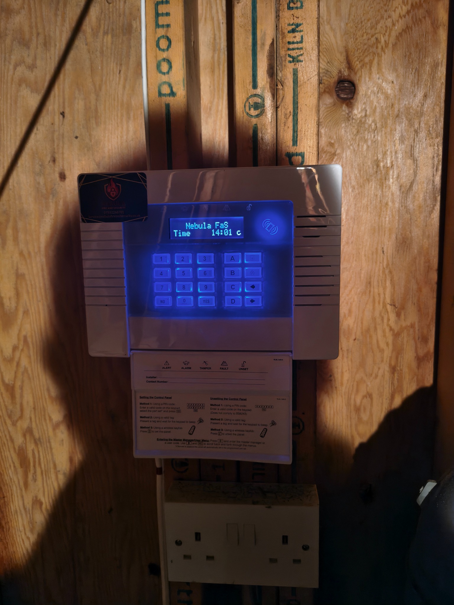 Illuminated intruder alarm control unit mounted on a timber board
